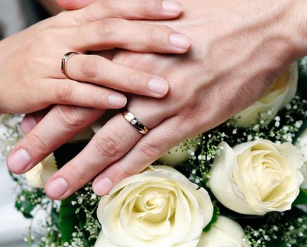 Closeup of newlywed couple holding hands over bouquet of flowers.