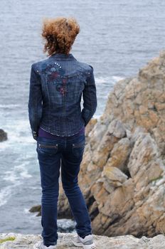 Young curly woman watching the coast and ocean of brittany, france.