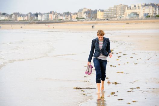 Young woman walking barefoot on french beach