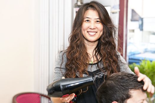 Smiling hairstylist drying hair with hairdryer in her salon