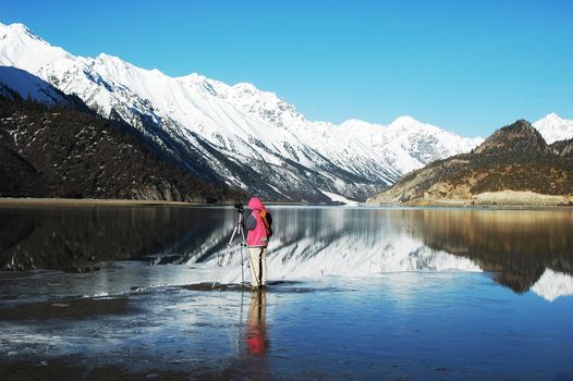 Landscape of snow-capped mountains with a photographer taking photos in the lake