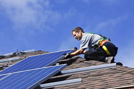 Man installing alternative energy photovoltaic solar panels on roof