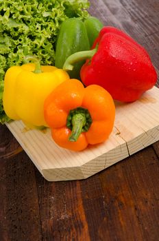 Yellow, red orange and green peppers, lettuce on wooden tray.