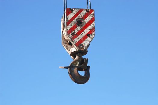 Detail of rusty crane hook and steel cables hanging on blue sky background