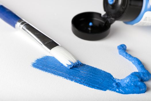 Blue acrylic paint with paint brush and tube of paint in the background