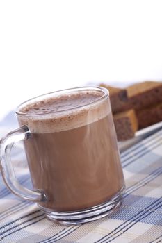 Fresh hot chocolate in glass mug with cake in background.