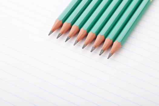 Eight green pencils on notebook paper.