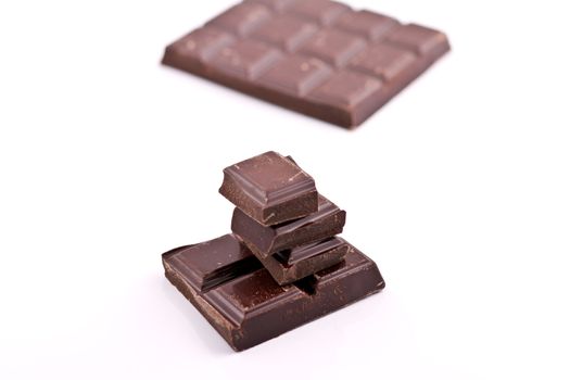 Stacked cholate pieces with chocolate block behind on white background