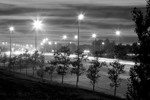 A photograph highway one at night with street lights and light streak from the headlights and taillights of passing cars