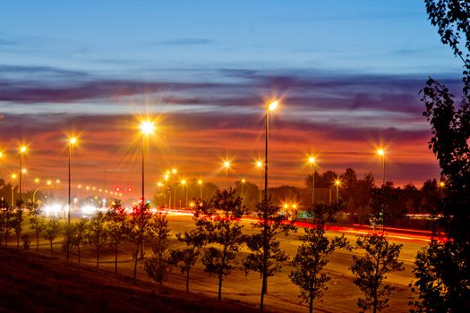 A photograph highway one at night with street lights and light streak from the headlights and taillights of passing cars