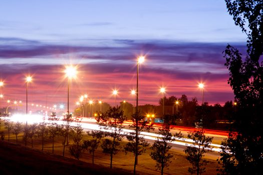 A photograph highway one at night with street lights and light streak from the headlights and taillights of passing cars