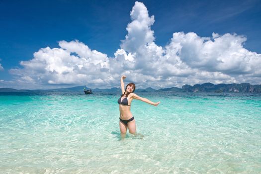 Young cheerful woman standing in the turquoise sea with her arms wide open 