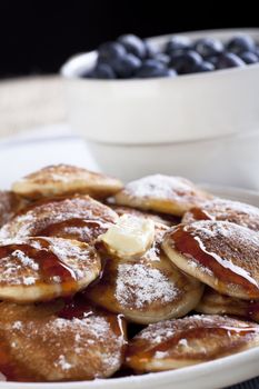 Dutch mini pancakes, or poffertjes, with butter, syrup and powdered sugar.  Fresh blueberries out of focus in the background.