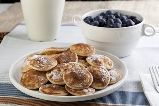Dutch mini pancakes, or poffertjes, with butter, syrup and powdered sugar.  Fresh blueberries out of focus in the background.