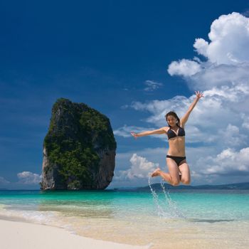 Young cheerful woman is jumping on the beach