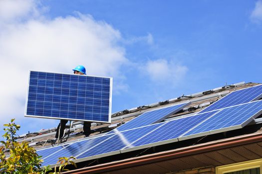 Worker installing alternative energy photovoltaic solar panels on roof