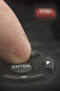 man finger pushing ENTER on a black remote control