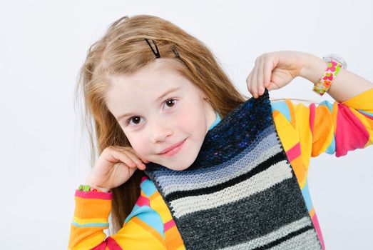 studio shot of pretty little girl trying on knitted scarf