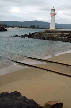 white lighthouse near sydney, rusty train rails leading into water