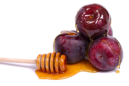Close up view of some violet plums with a honey dipper isolated on a white background.