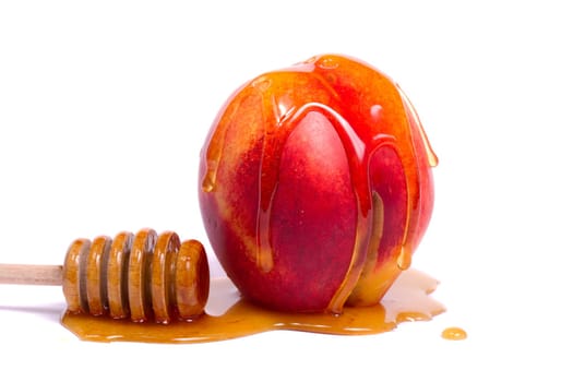 Close up view of a peach with a honey dipper isolated on a white background.