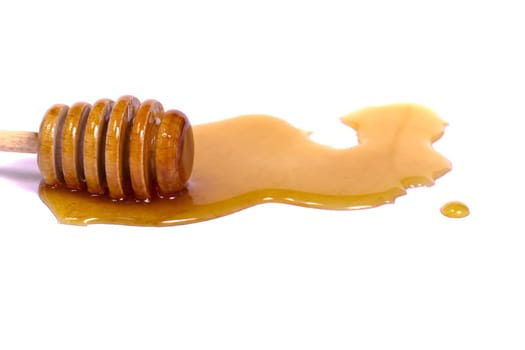 Natural honey spilled on a white background next to a honey dipper.