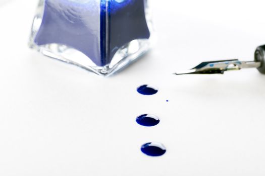 Ink drops on paper with calligraphy pen and bottle of blue ink.