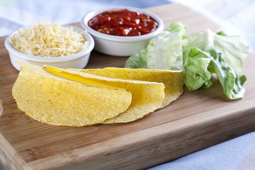 Taco ingredients: taco sauce, lettuce, taco shells and shredded cheese.