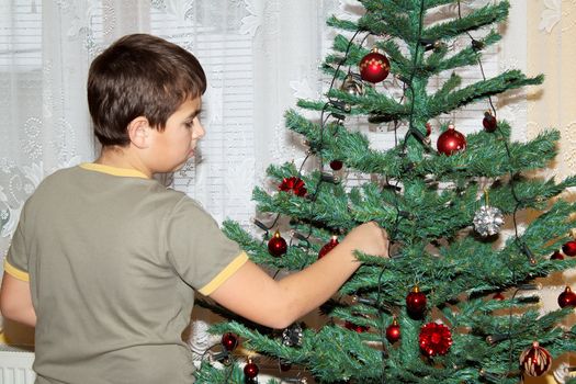 Young boy holding Christmas decorations on tree 