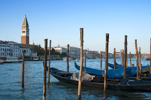 Traditional venetian gondlolas and St Mark's Campanile over blue sky in Venice, Italy