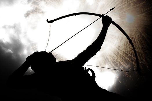 A silhouette of an archer, on the backdrop of a sky with exploding gun powder.