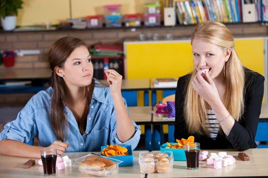 Two schoolgirls in classroom eating snacks for lunch