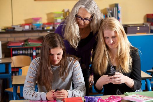 Two schoolgirls showing the teacher what is on their phones