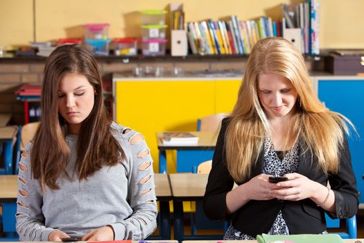 Two teenage girls playing with their phones in the classroom
