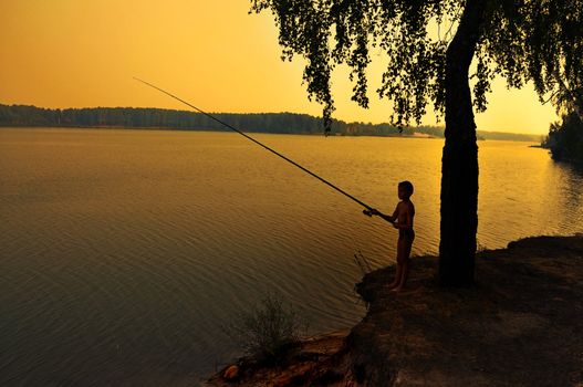 fishing on shoreline at dusk during a sunset.