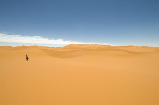 Woman walking alone among the sand dunes of the Sahara desert. Best of Morocco.