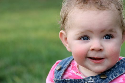 Girl toddler with quirky grin in pink and blue with green grass