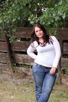 Young woman standing in field with brown wood fence and trees