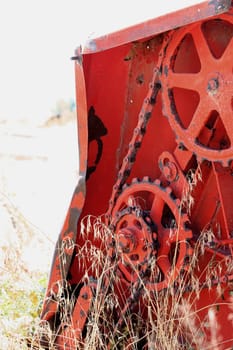 Piece of forgotten orange equipment with weeds and grass growing around it.