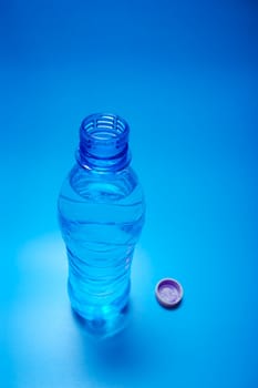 Open bottle of water on blue background