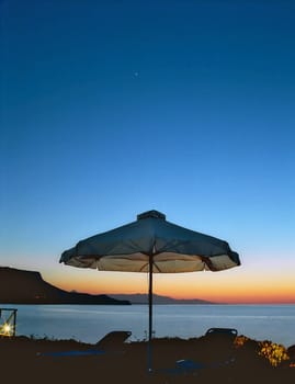 A sunshade with sunbeds are against of a picturesque sunset in Crete, an early star shines heaven-hight 