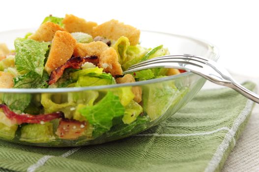 Fresh caesar salad with croutons and bacon bits served in a glass bowl