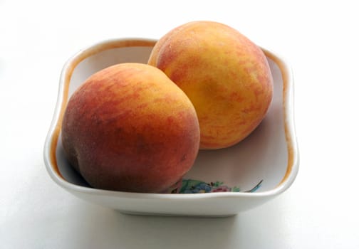 two peaches in the saucer on white table.