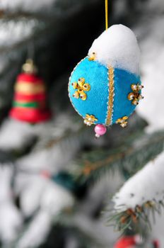 Christmas ornaments hanging on snow covered spruce tree outside