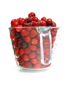 Fresh red cranberries in a glass measuring cup on white background