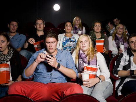 Mindless man with cellphone together with his girlfriend at the movie theater