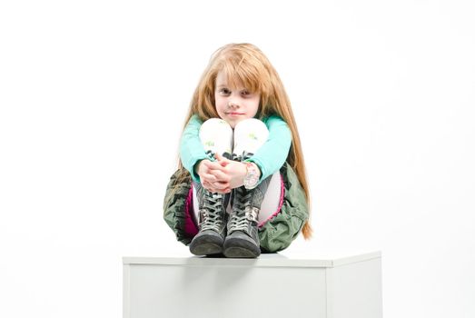 studio shot of pretty little girl sitting on a white cube