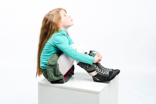 studio shot of pretty little girl sitting on a white cube