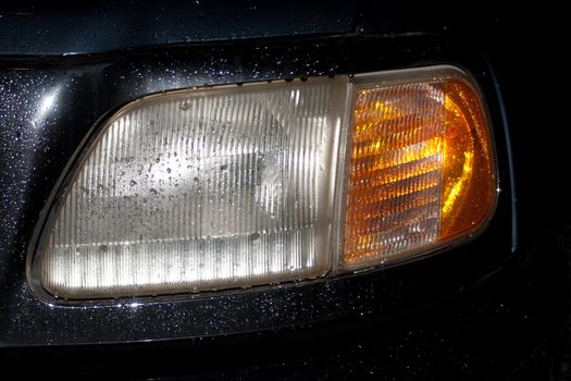Headlight of an SUV in the rain by night with water