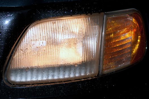 Headlight of an SUV in the rain by night with water